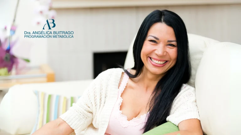 Mujer adulta sentada en un sofá claro, sonriendo con expresión cálida. En la parte izquierda de la imagen aparece el logo de la Doctora Metabolismo