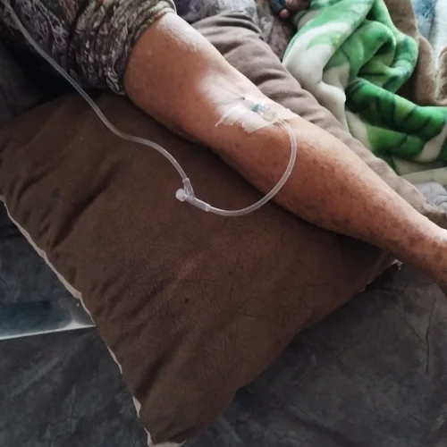 Paciente recibiendo sueroterapia en casa, con vía intravenosa en el brazo y descansando sobre un sofá. Doctora metabolismo